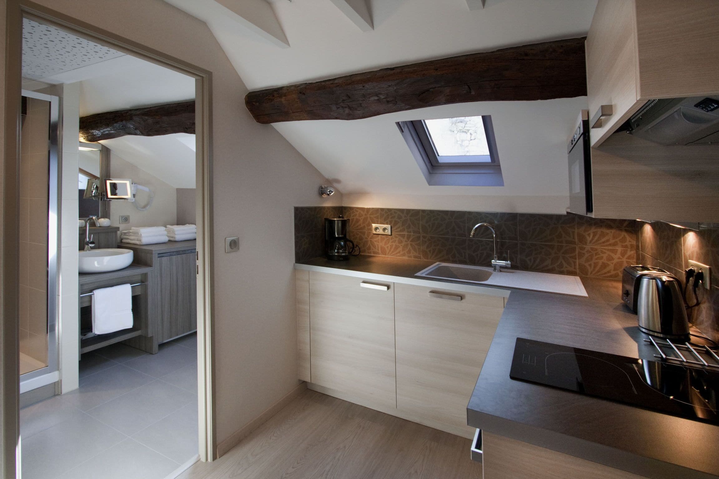 A modern kitchen with a skylight, wooden beams, and a large island with a sink.