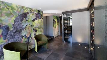 A modern interior with a wine rack, two green chairs, and a mural of grapevines.