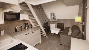 Un espacio habitable compacto con cocina, escalera, sofá y un pequeño comedor.