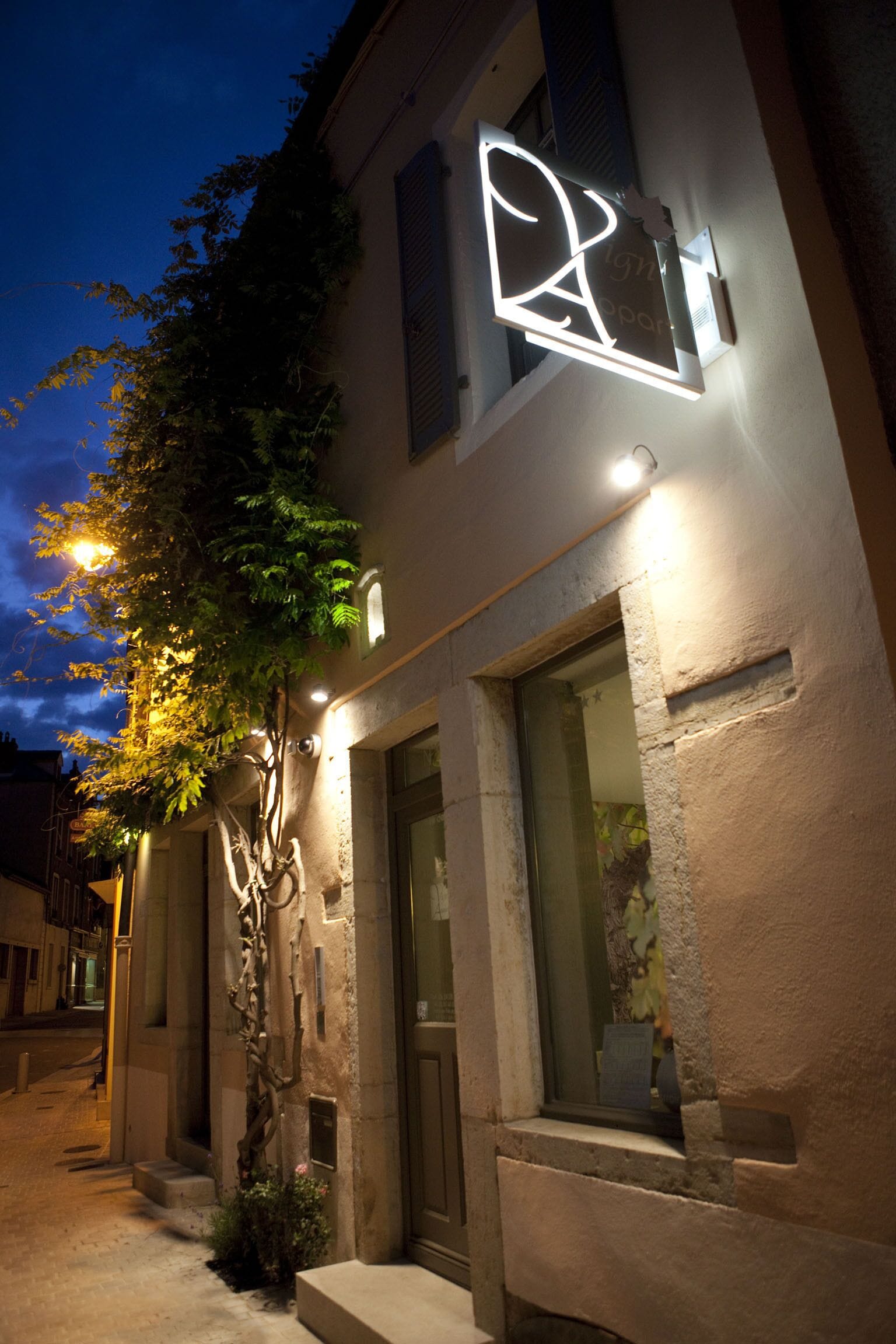Ein Gebäude mit moderner Fassade, einem gut sichtbaren Eingang und einem Baum davor.