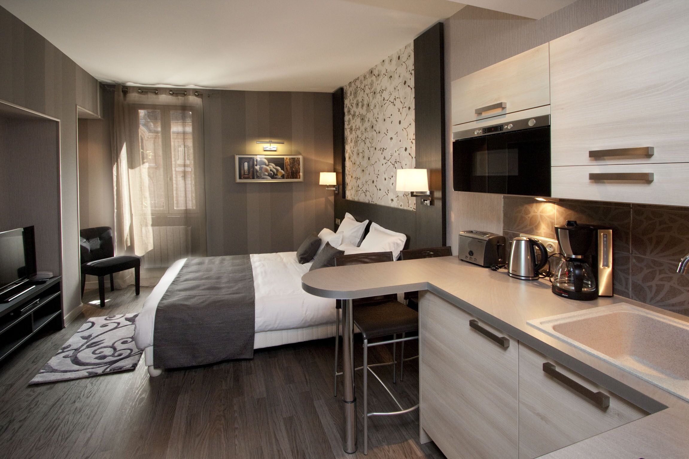 Habitación de hotel con cama, escritorio, microondas, cafetera y televisor.