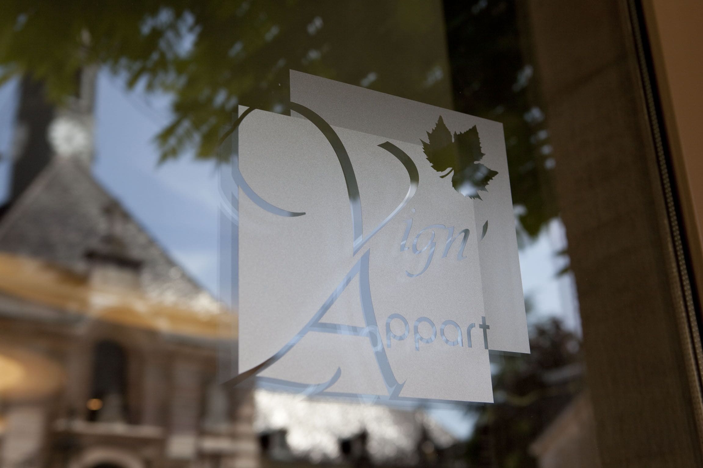 Un panneau portant l’inscription « Sign Appart » est partiellement masqué par une branche d’arbre.
