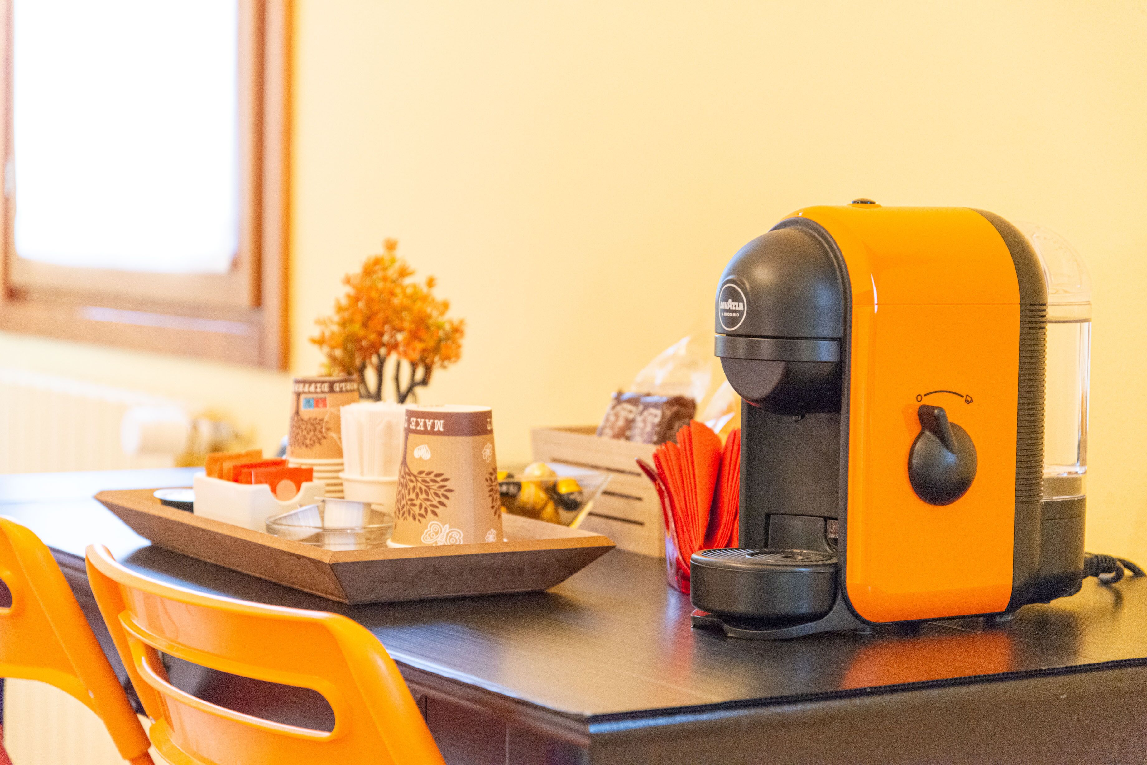 A coffee maker on a table with a tray, a small tree decoration, and a window in the background.
