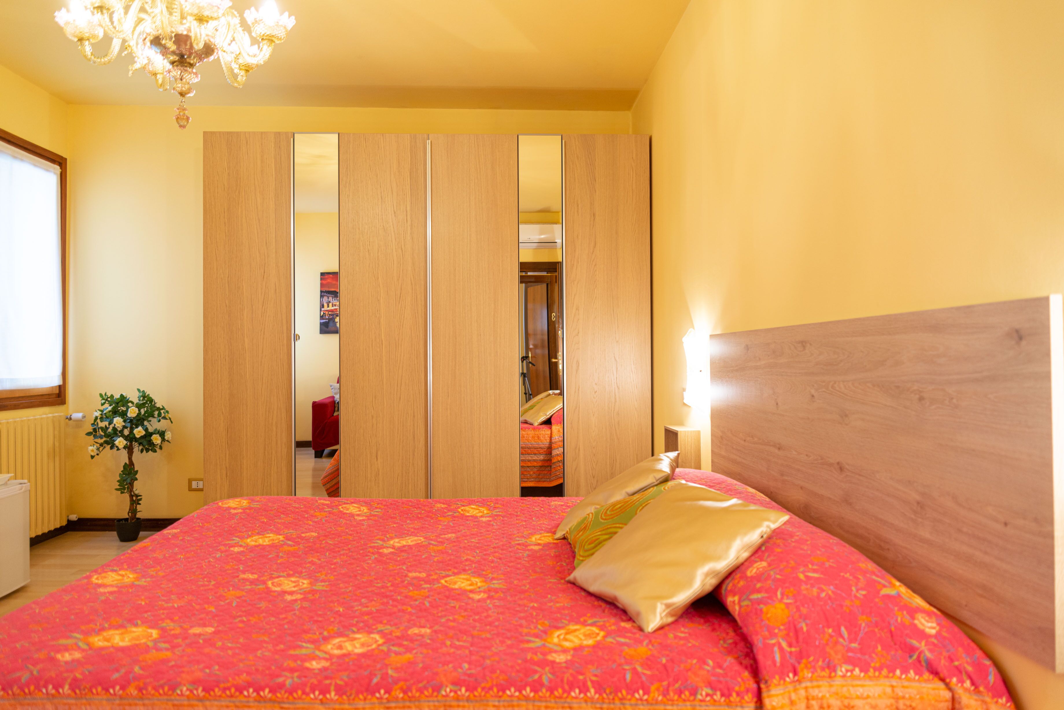Une chambre d’hôtel avec un grand lit, une armoire en bois et une plante en pot.