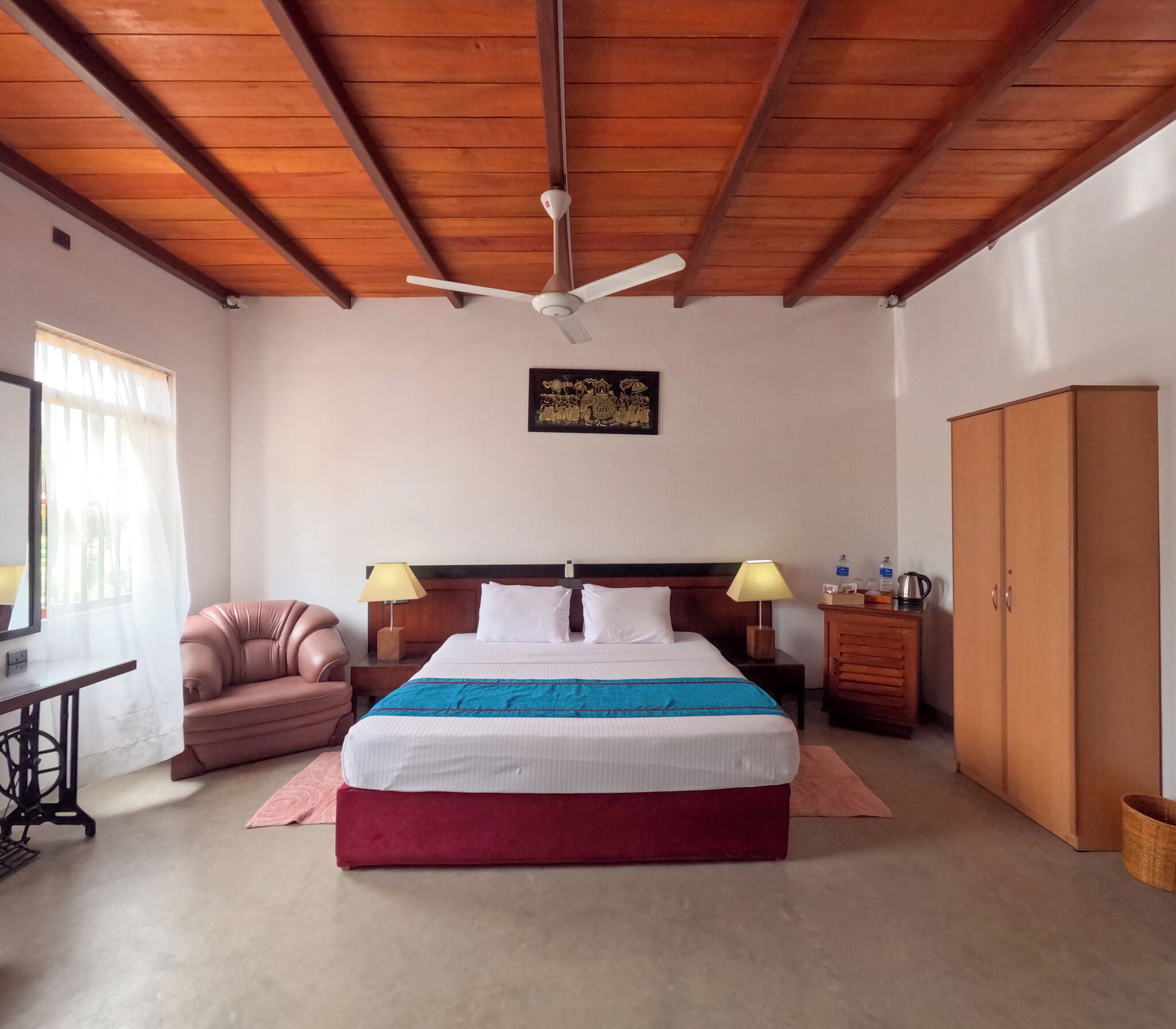 Un dormitorio con cama, ventilador de techo, armario de madera, escritorio con silla y ventana con cortinas.