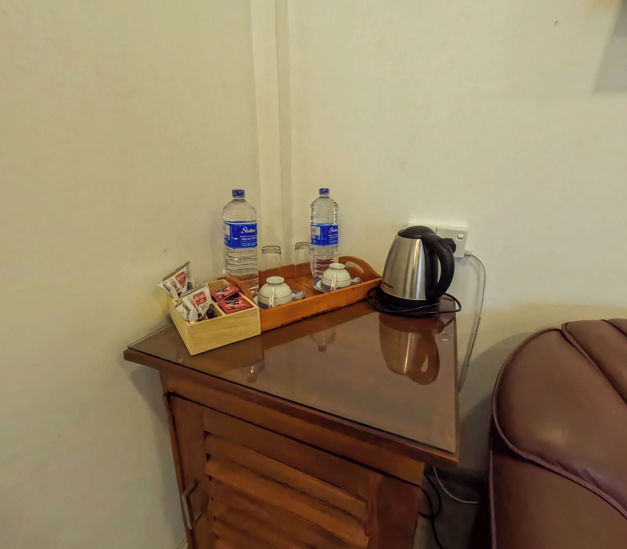 Una pequeña mesa de madera con un hervidor, dos botellas de agua y una bandeja con bolsitas de té y una tetera.