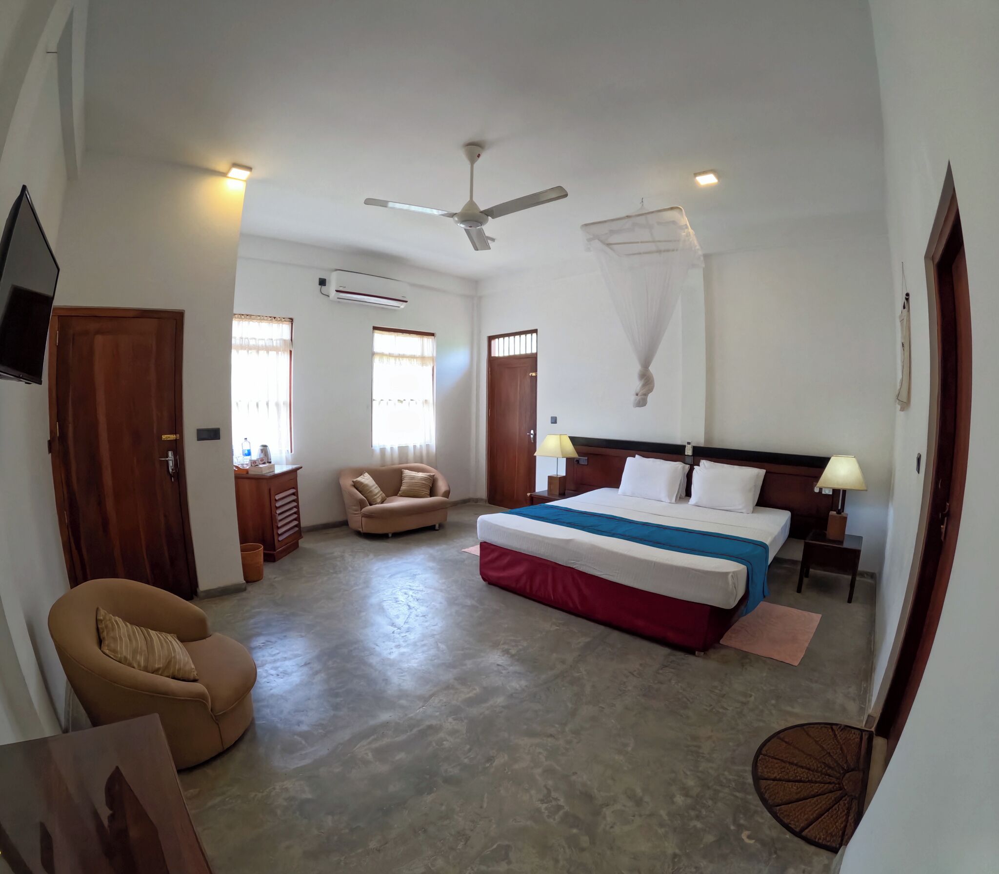 A spacious hotel room with a large bed, a ceiling fan, a sitting area with a chair, and a small table.