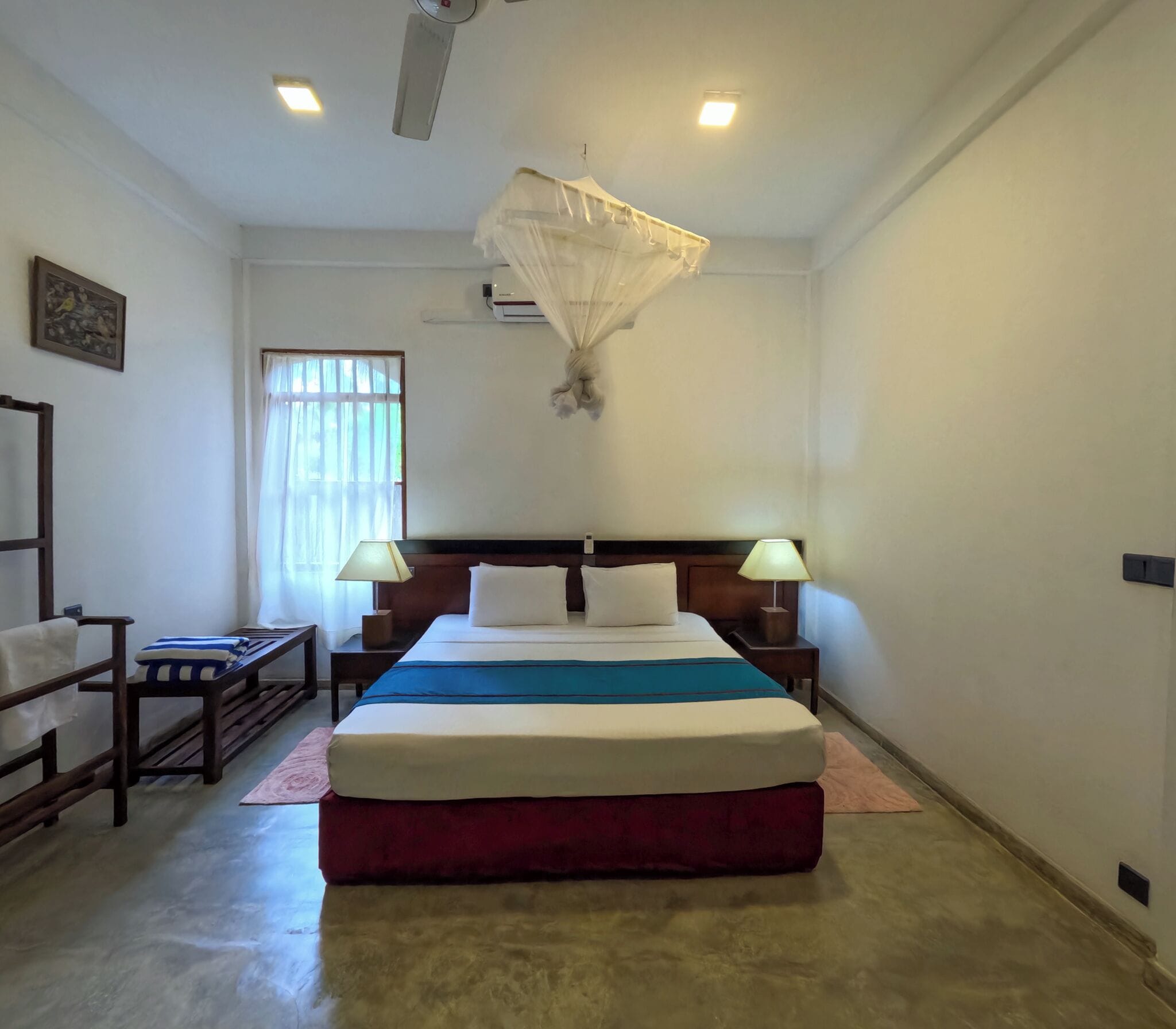 Une chambre d’hôtel avec un grand lit, deux lampes de chevet, une fenêtre avec des rideaux, un ventilateur de plafond et un climatiseur fixé au mur.