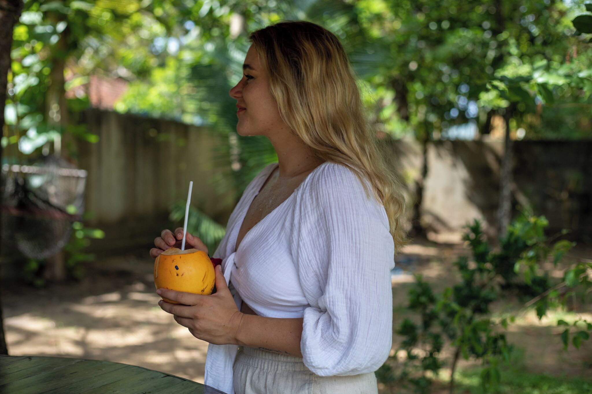 Iemand houdt een drankje met rietje vast, staand buiten met groen in de achtergrond.