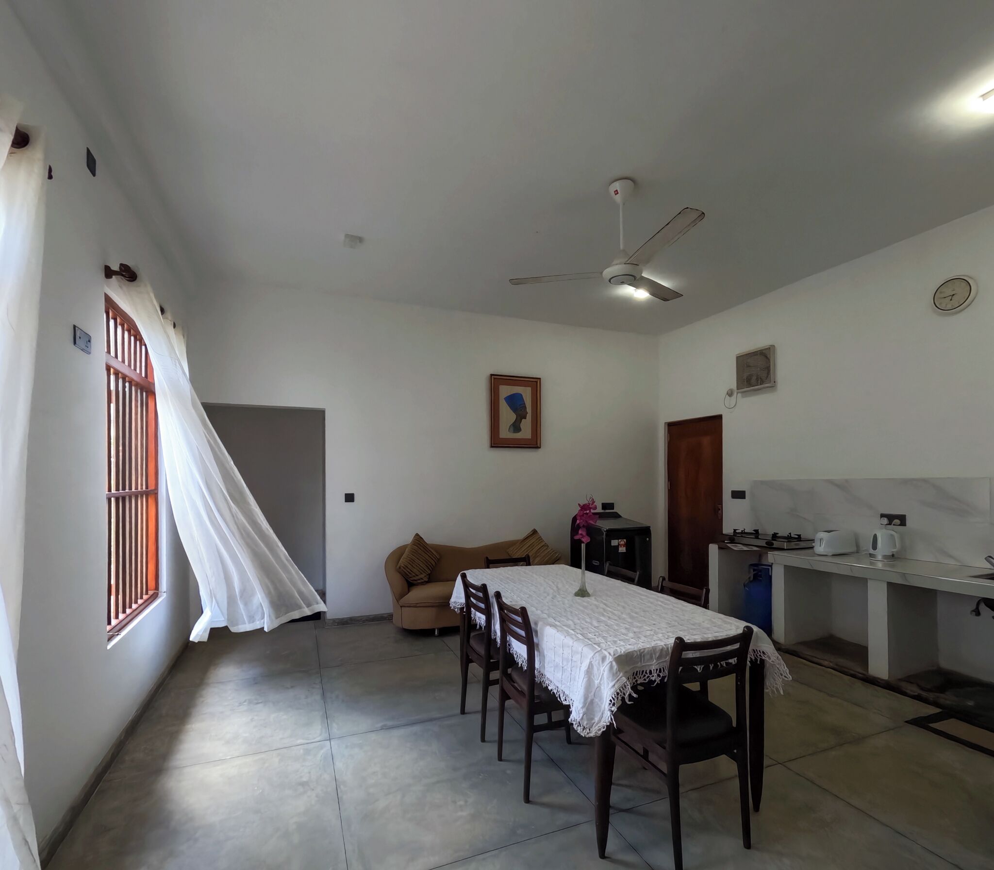 Un coin repas avec une table dressée pour quatre personnes, un canapé, un ventilateur de plafond et une fenêtre avec des rideaux.