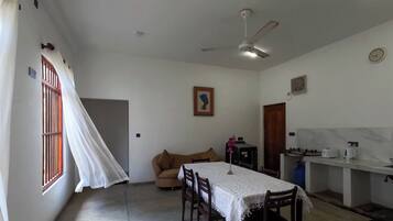 A dining area with a table set for four, a sofa, a ceiling fan, and a window with curtains.