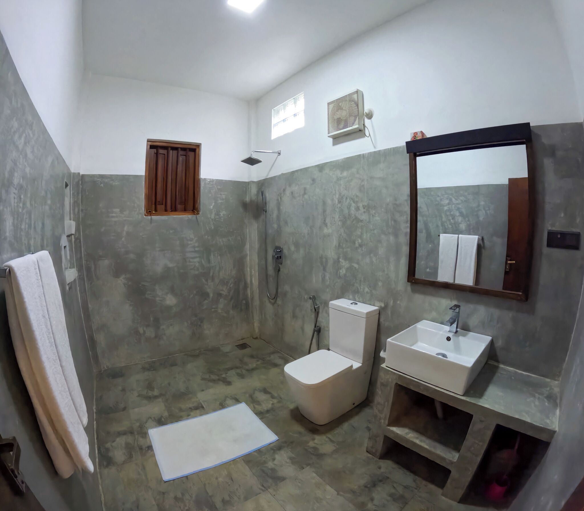 Baño con ducha, inodoro, lavamanos y un espejo grande.