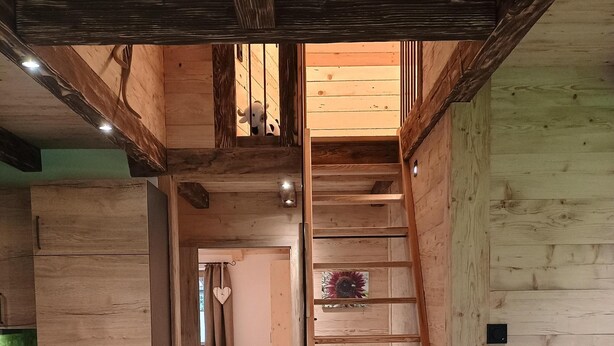 Ein Holzinnenraum mit einer zentralen Treppe, Holzwänden und einer Küchenzeile mit Schränken und einer Arbeitsplatte.