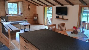 Ein gemütliches Blockhauszimmer mit Holzvertäfelung, einer Couch, einem Esstisch und einem an der Wand befestigten Fernseher.