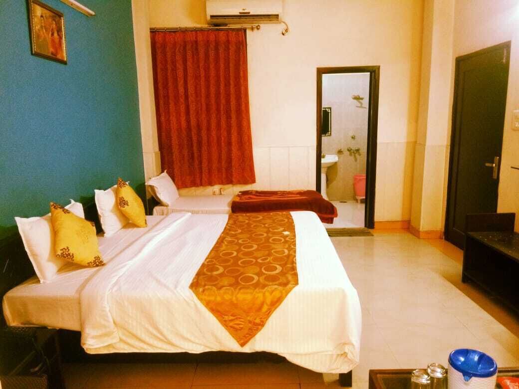 Una camera d'albergo con due letti, una tenda rossa, un bagno con un lavandino e una porta.