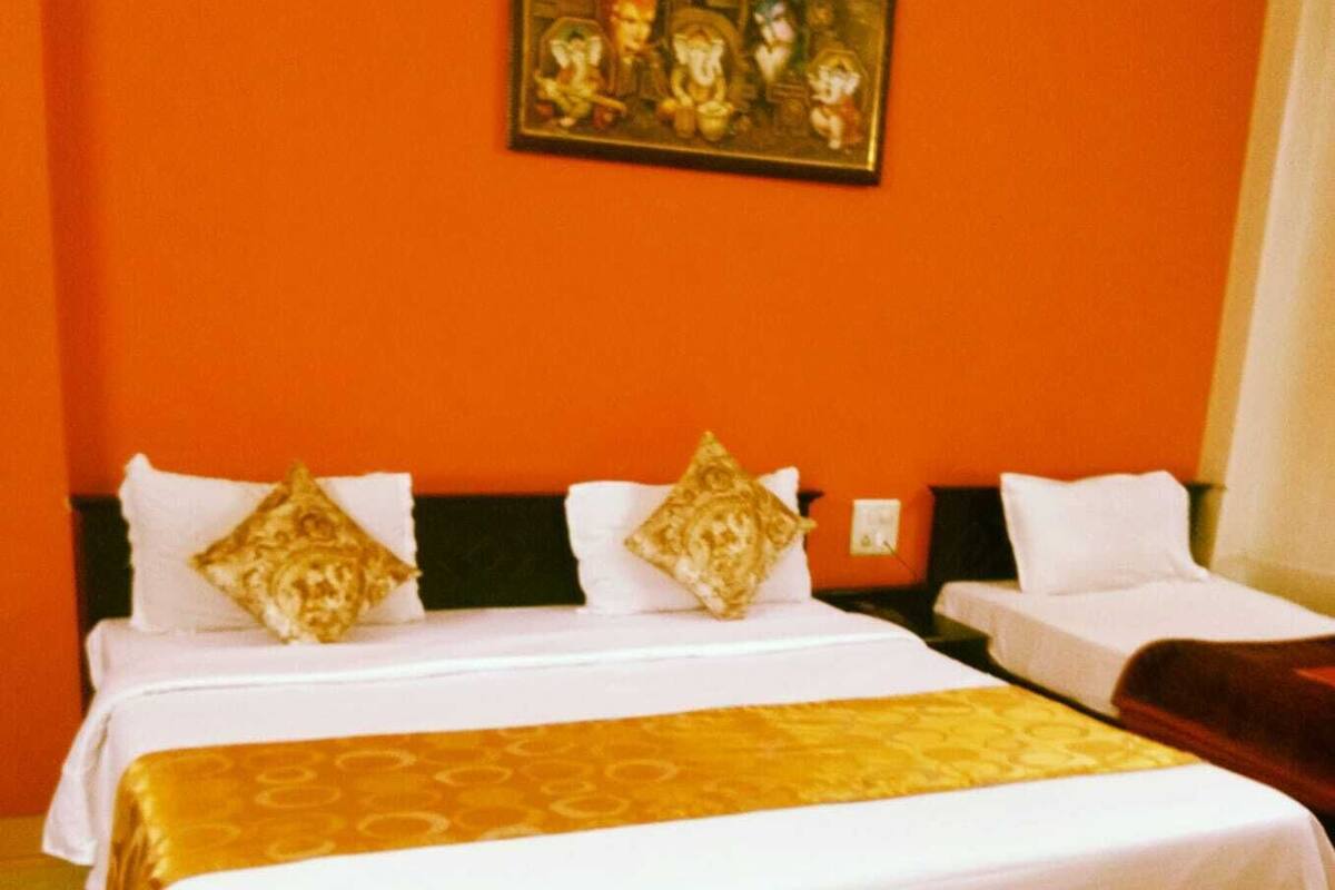 A hotel room with two beds, a large painting on the wall, and a bright orange wall.