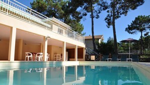 A swimming pool with lounge chairs and a covered area with tables and chairs.