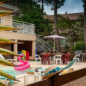 Un espace piscine aménagé avec des chaises longues, une table et un barbecue.
