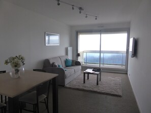 Relax in a spacious living room with a large window offering a view of the outdoors, a flat-screen TV, and a comfortable seating area.