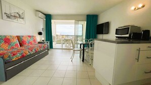 Un espacio habitable compacto con sofá, mesa de comedor con sillas, kitchenette y balcón con vistas.