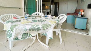 Un comedor con una mesa cubierta con un mantel estampado con motivos de hojas, rodeado de sillas blancas.