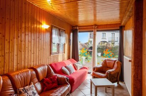 A wooden interior with a leather sofa, a small table, and a view of a garden through a glass door. - Homerez - House Girmont-Val-d'Ajol, mountain view (Girmont-Val-d'Ajol)