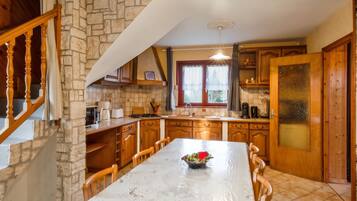 A kitchen with a stone wall, wooden cabinets, a dining table with chairs, and a window with curtains.