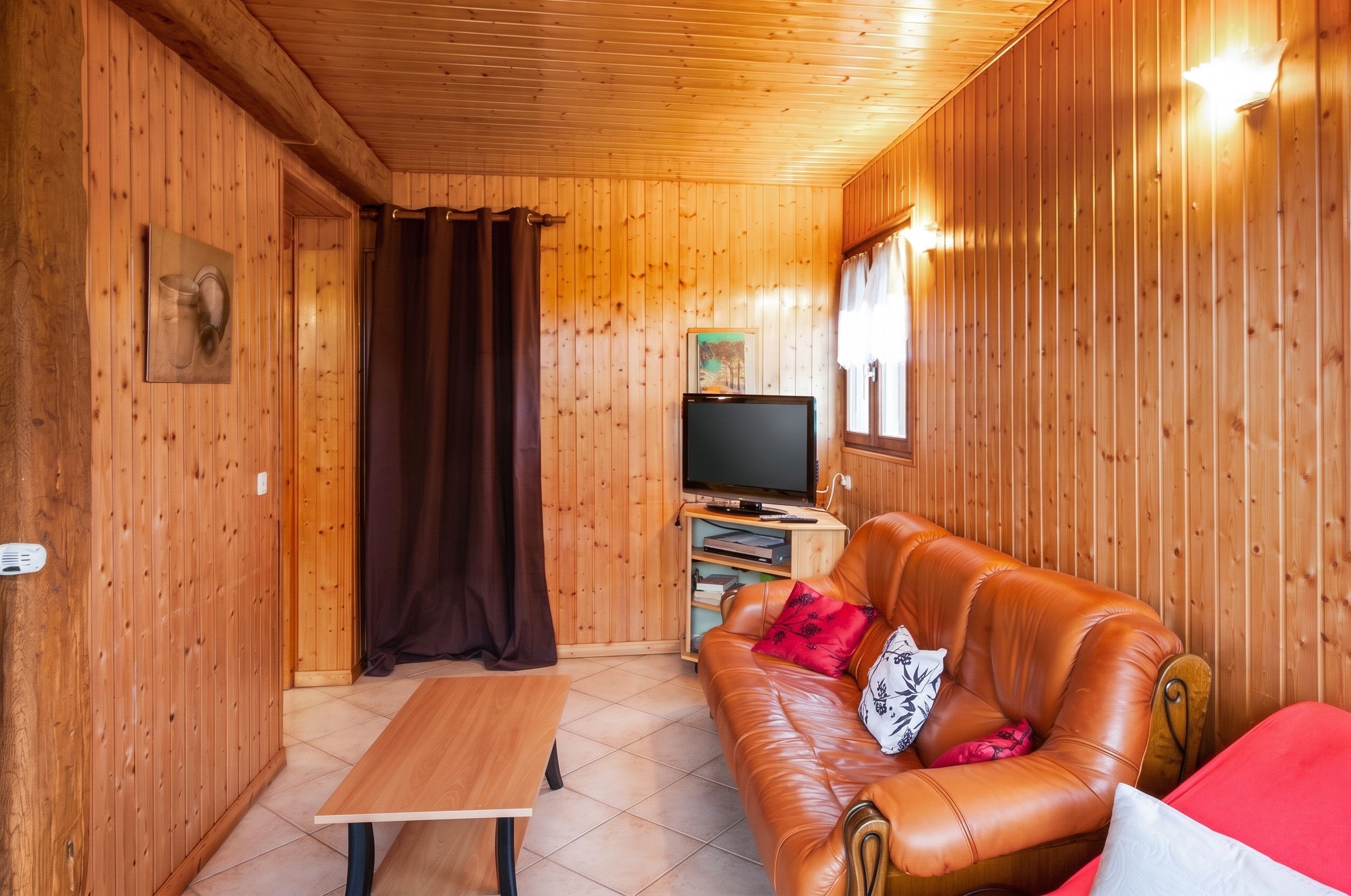 Une pièce aux murs lambrissés, avec un canapé en cuir, une table en bois et un téléviseur.
