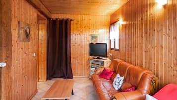 Une pièce aux murs lambrissés, avec un canapé en cuir, une table en bois et un téléviseur.