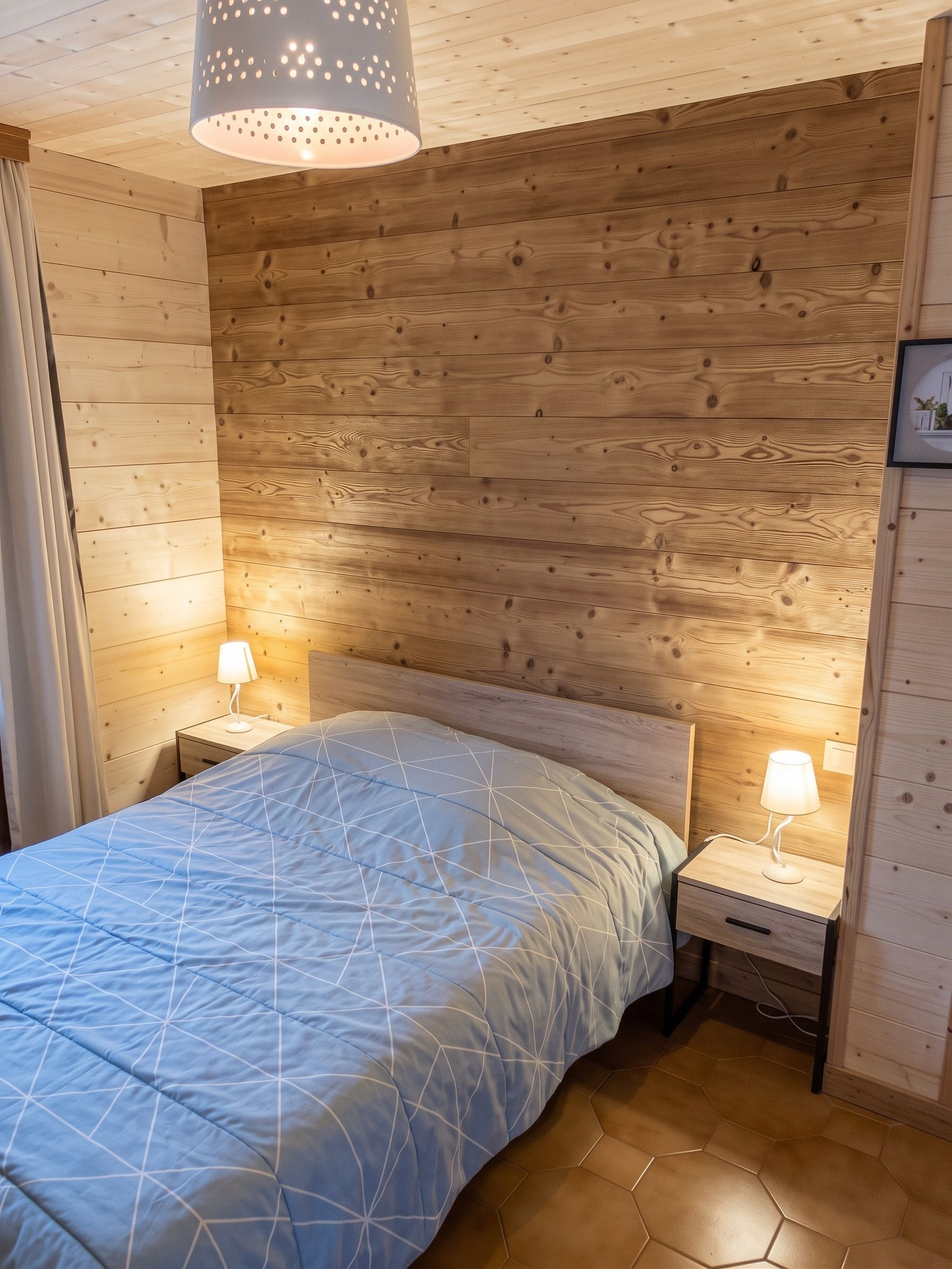 Une chambre à coucher avec une tête de lit en bois, un lit recouvert d’une courtepointe bleue, deux lampes de chevet et un luminaire suspendu.