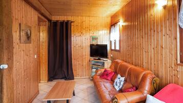 Een kamer met houten lambrisering, een leren bank, een houten tafel en een televisie.