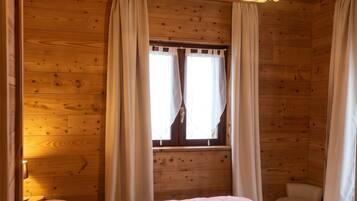 Une chambre dans une cabane en bois, avec un lit, des rideaux, une fenêtre et un luminaire suspendu.