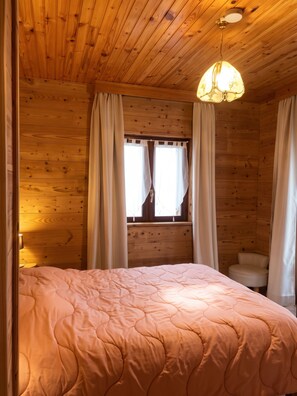 Un dormitorio de cabaña de madera con cama, cortinas, una ventana y una lámpara colgante.