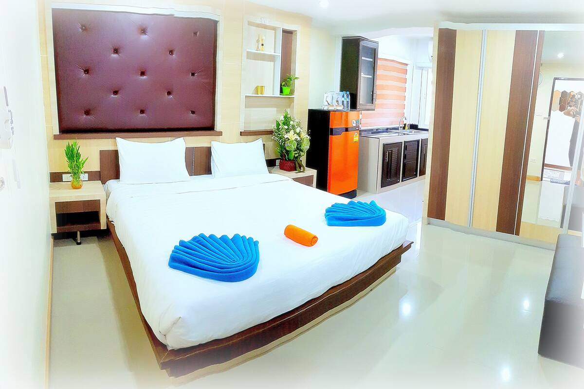 A hotel room with a large bed, a TV, a minibar, and a kitchenette.