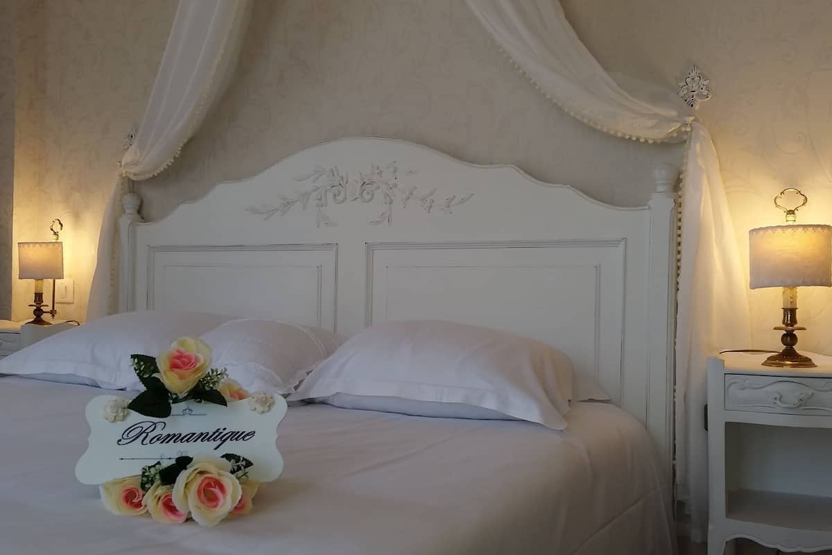 A neatly made bed with white linens, two bedside tables with lamps, and a decorative headboard with floral carvings.