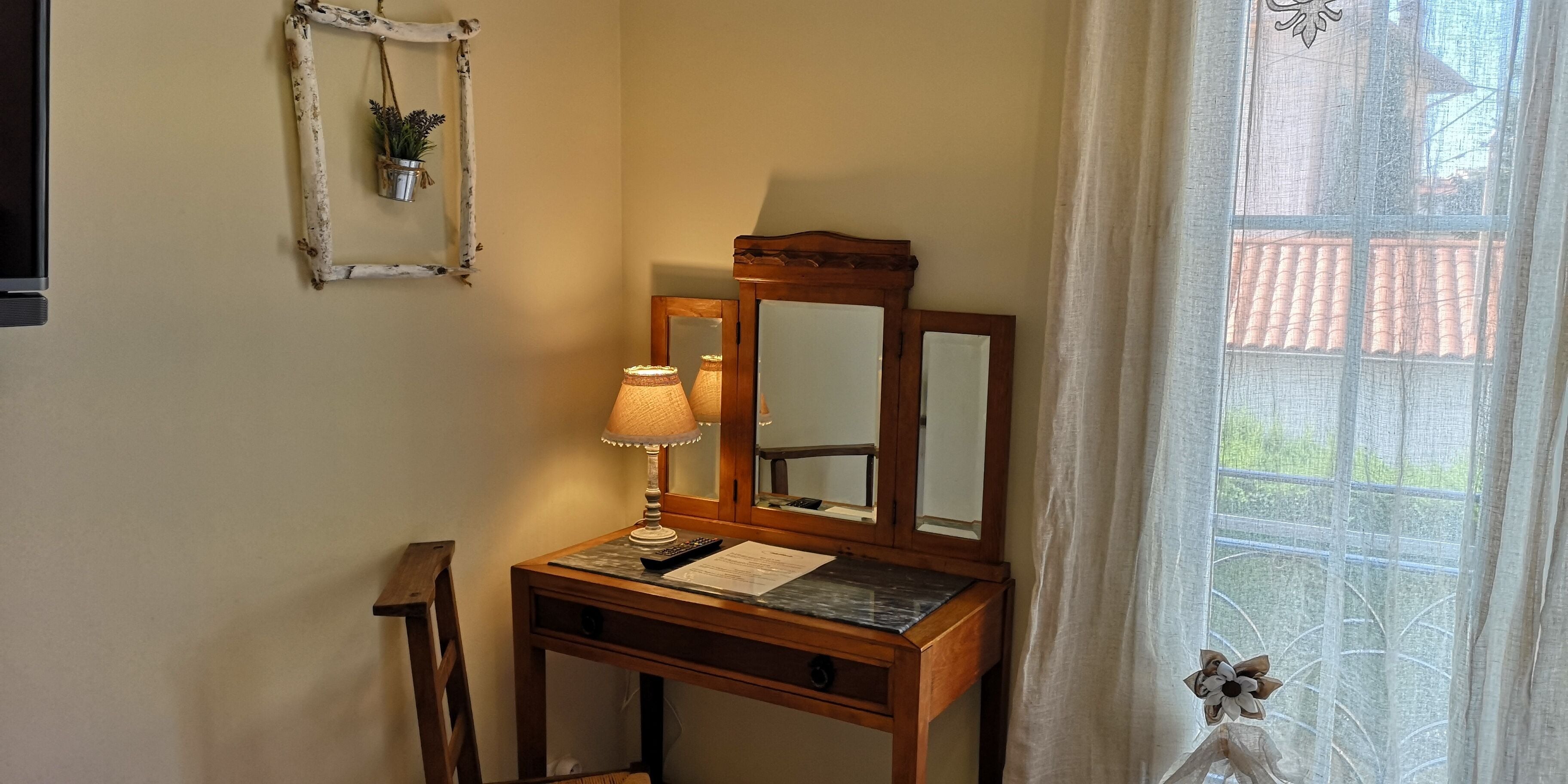 Een houten bureau met een lamp, een spiegel en een plant aan de muur.