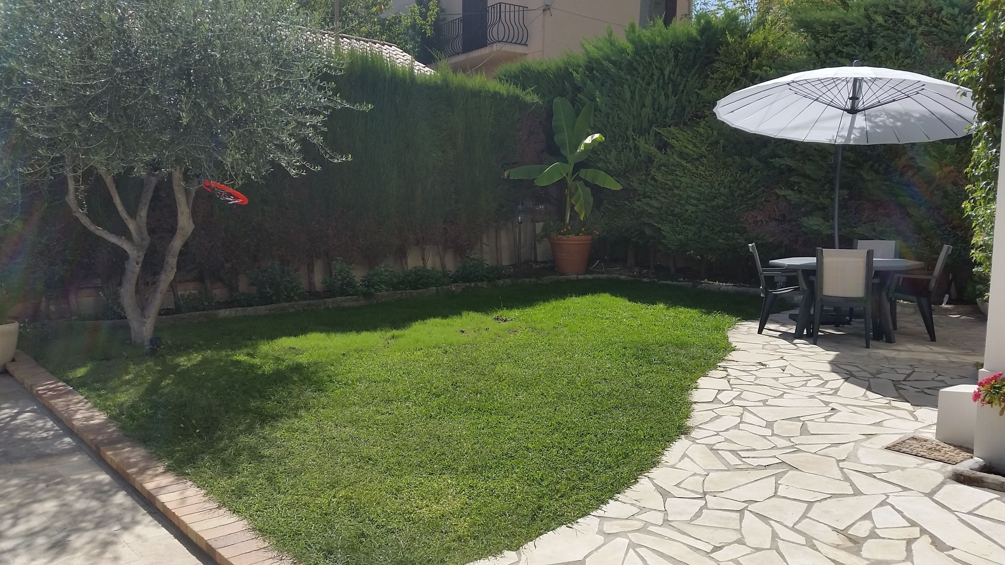 A patio area with a stone-tiled floor, a small lawn, and a table with chairs.