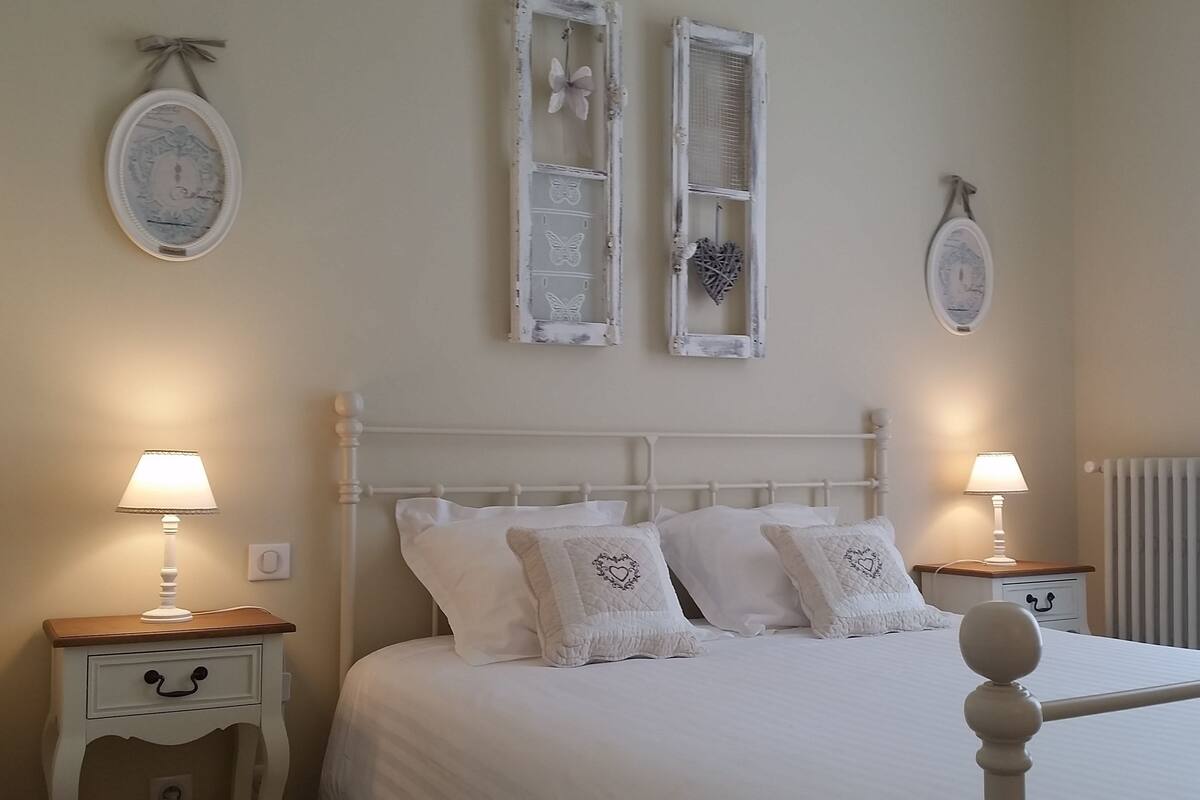 A bedroom with a white bed, two bedside tables with lamps, and decorative wall mirrors.