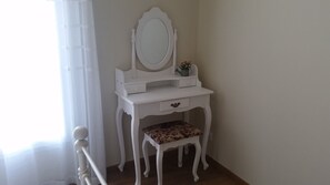 A white vanity with a mirror, a small drawer, and a floral-patterned stool.