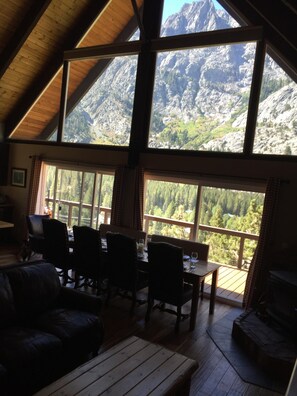 A cozy living room with a high ceiling and large windows overlooking a mountainous landscape.