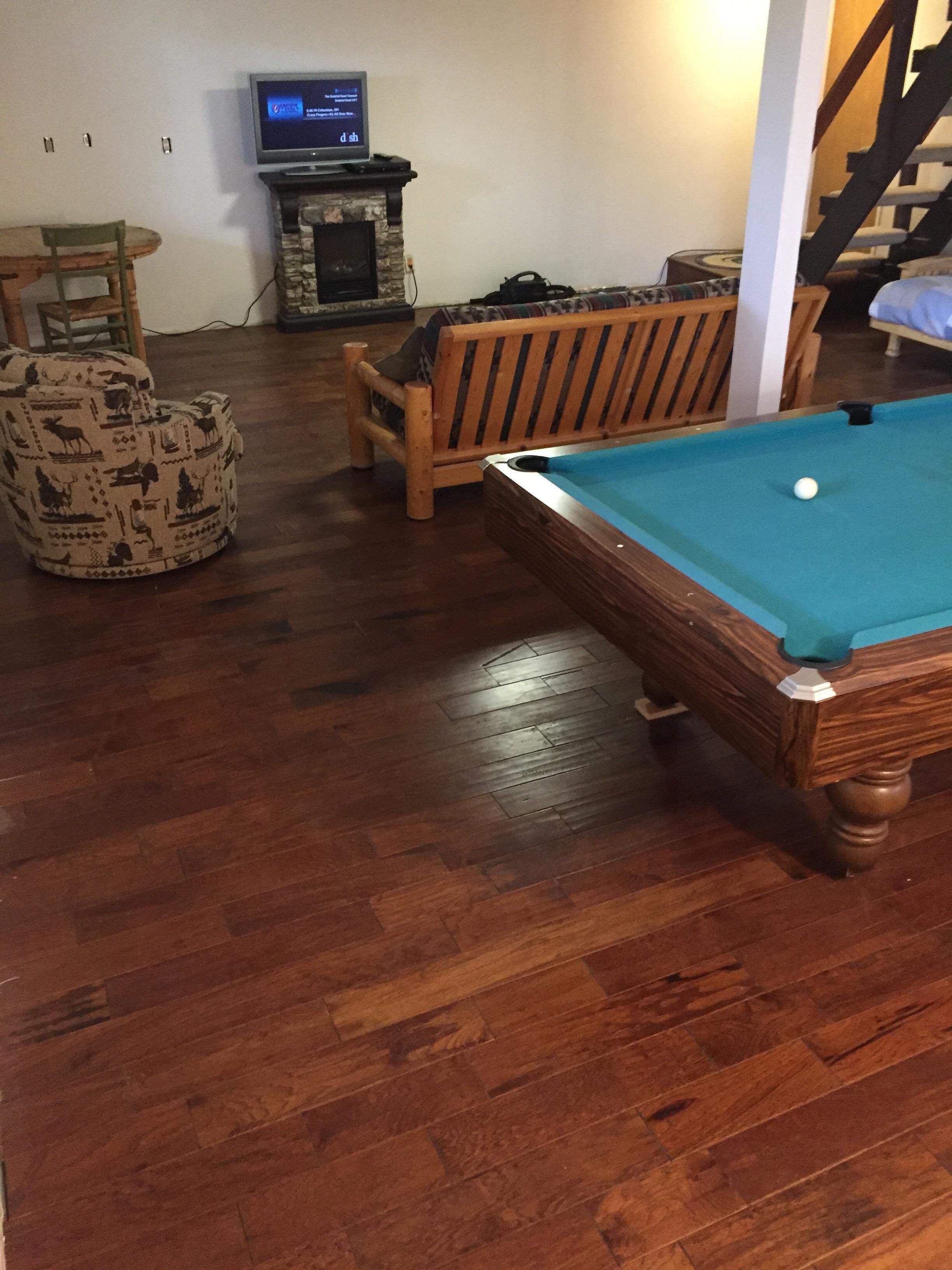 A wooden pool table in a living room with a television and a fireplace.