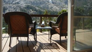 Een balkon met twee rieten stoelen en een kleine tafel, met uitzicht op een bergachtig landschap.