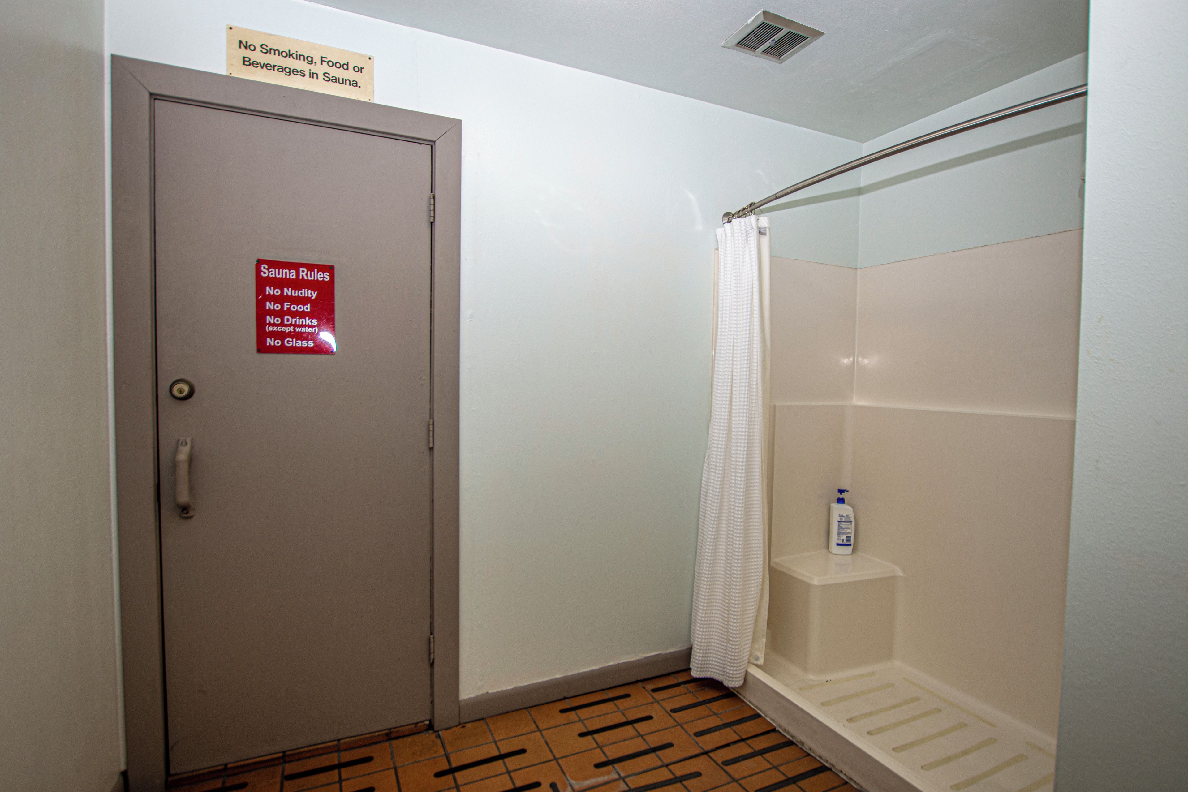Un baño con ducha, un cartel con las normas de la sauna y una botella de champú en un estante.