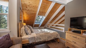 Une chambre avec un plafond en pente, un lit, une télévision et une commode.