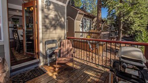 Une terrasse en bois avec un barbecue, une chaise et une porte donnant sur une pièce qui comprend un coin cuisine.