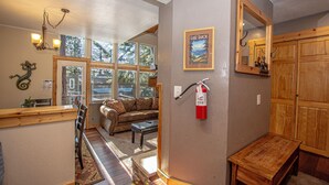 Un salon chaleureux avec une cheminée, un banc en bois et une grande fenêtre donnant sur l’extérieur.