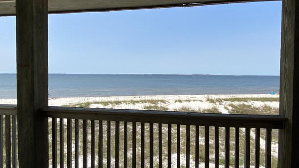 A view through a wooden railing of a beach with sand and sparse vegetation. - 213 Seashack- Your Dream Beach Retreat, Steps from the Shore (St Joe Beach)