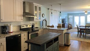 A modern kitchen with white cabinetry, a central island, and a dining area with a table and chairs. - 213 Seashack- Your Dream Beach Retreat, Steps from the Shore (St Joe Beach)