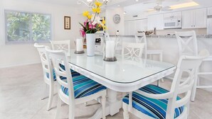 Une cuisine moderne avec des meubles blancs, une table à manger au plateau en verre et des chaises à rayures bleues.