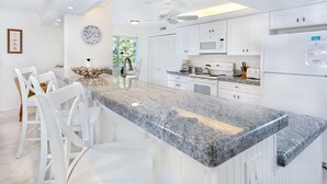 Une cuisine moderne avec des meubles blancs, un plan de travail en granit et un ventilateur de plafond.